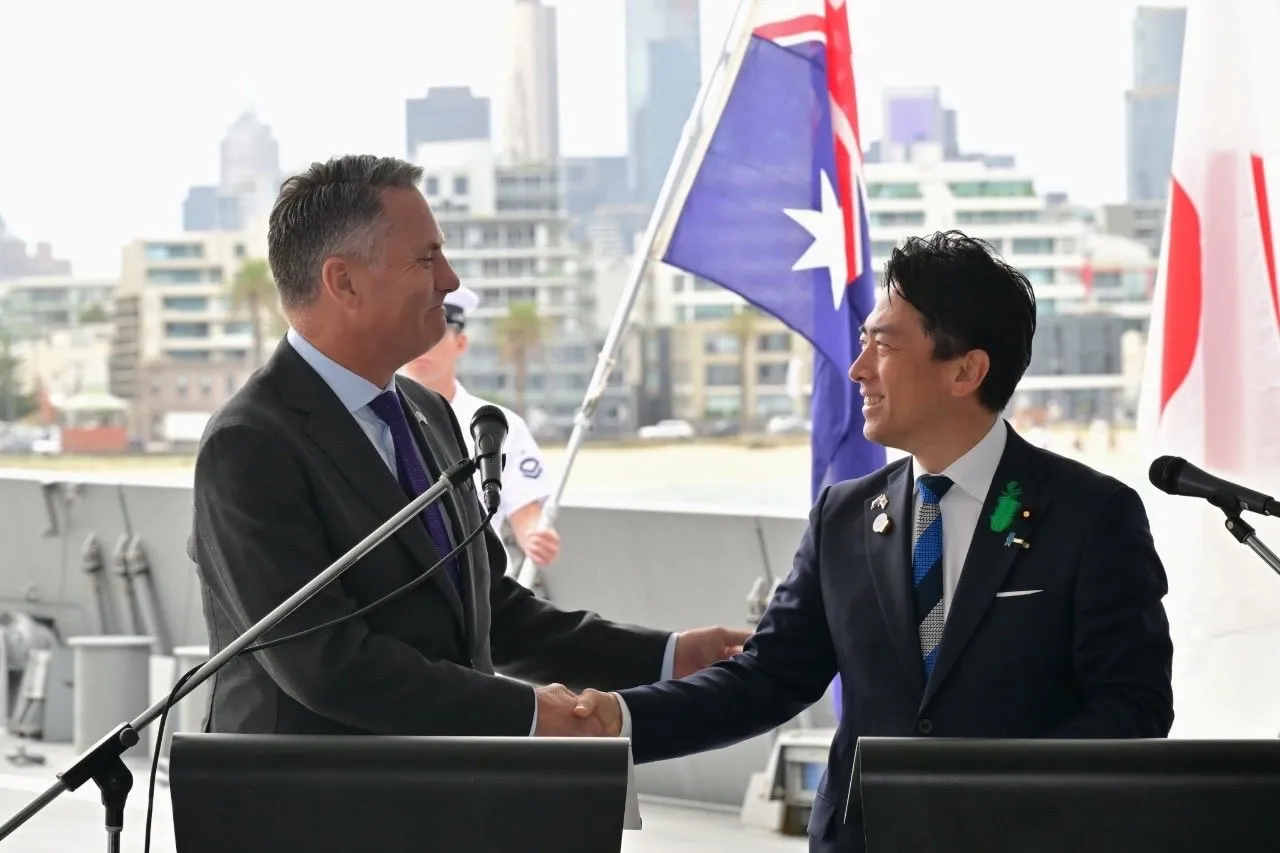 Two defence ministers in suits stand together on the deck of a grey Japanese warship