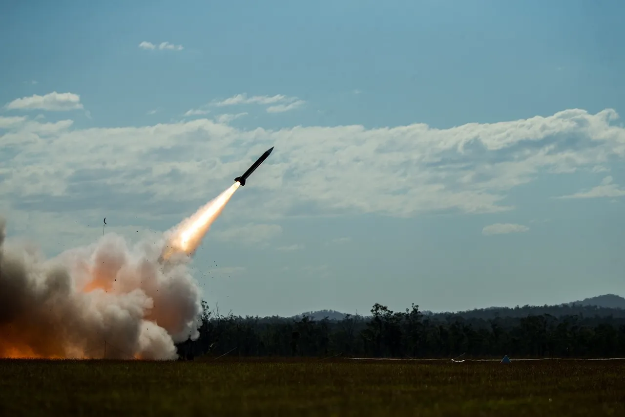 A surface-to-air missile climbs into a blue sky trailing flame and smoke above a grass field and tree line