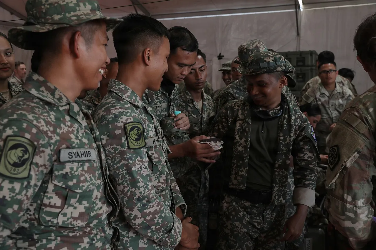 Malaysian Army soldiers in camouflage uniforms gather inside a tent to examine a filled blood bag during field medical training