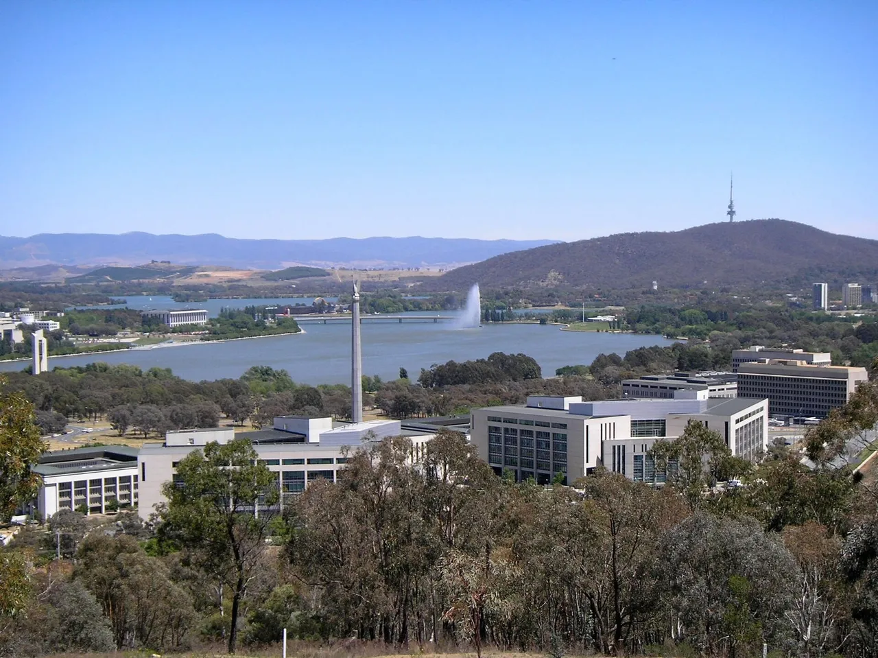 A cluster of grey office buildings surrounded by trees in Canberra, seen from a nearby hill