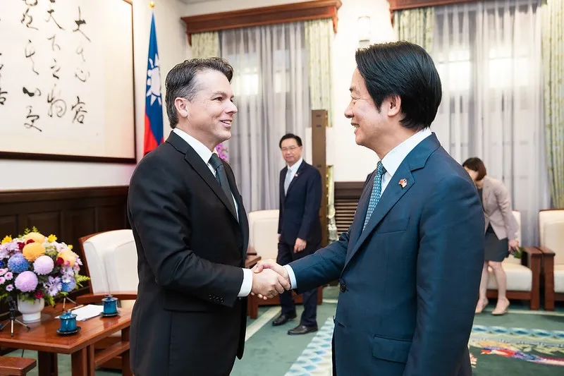 Taiwan's President Lai Ching-te, in a blue suit, shakes hands with a smiling US congressman in a dark suit in a reception room with a Taiwanese flag and calligraphy on the wall.