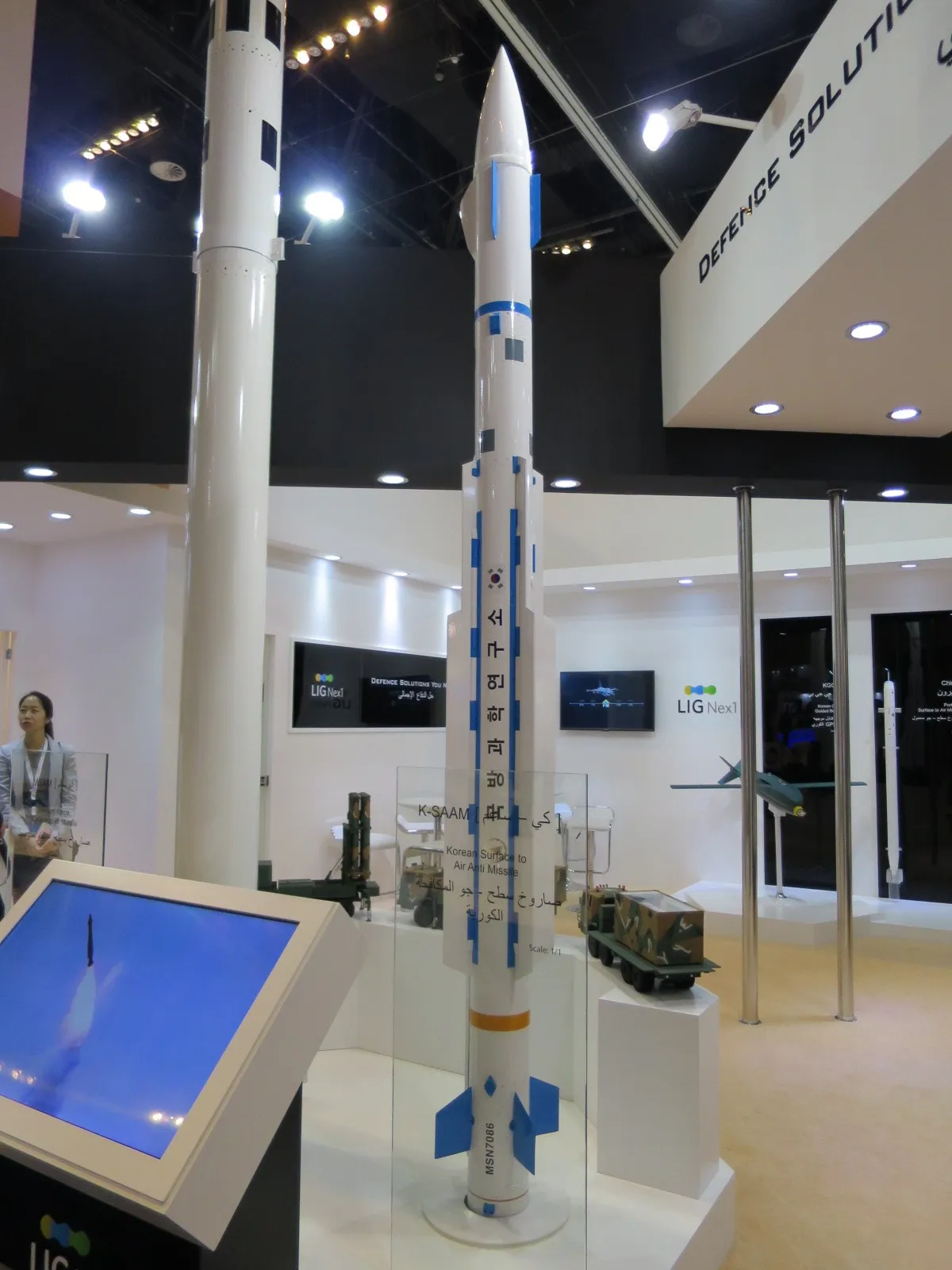 A grey missile mock-up standing upright on a display stand at an indoor defence exhibition