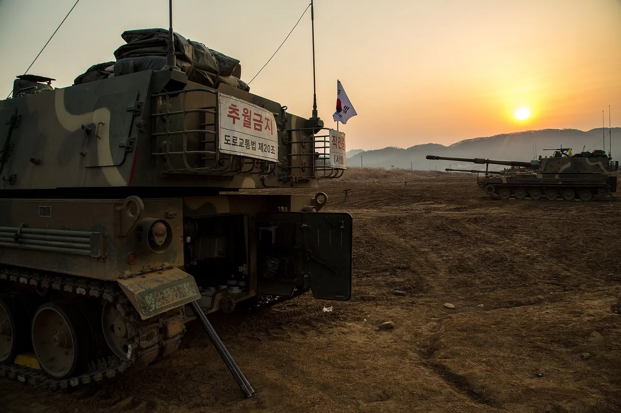 Two camouflaged South Korean K9 self-propelled howitzers on a dirt range at sunset, one seen from behind with a South Korean flag on its turret