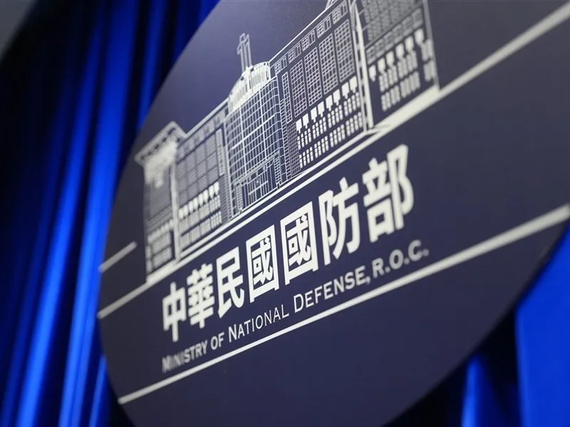 Close-up of the round Ministry of National Defense emblem against a blue curtain
