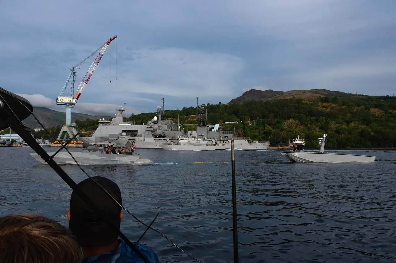 A US Navy special warfare assault craft tows a grey MARTAC T-38 Devil Ray uncrewed surface vessel across Subic Bay