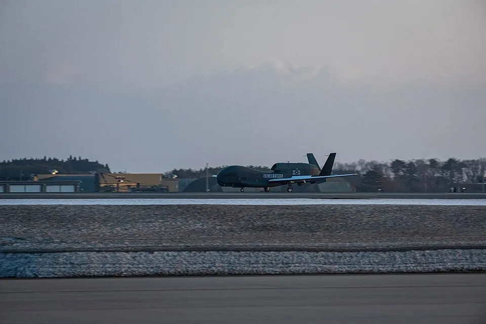 A dark grey RQ-4B Global Hawk drone with long straight wings rolling along a runway at dusk