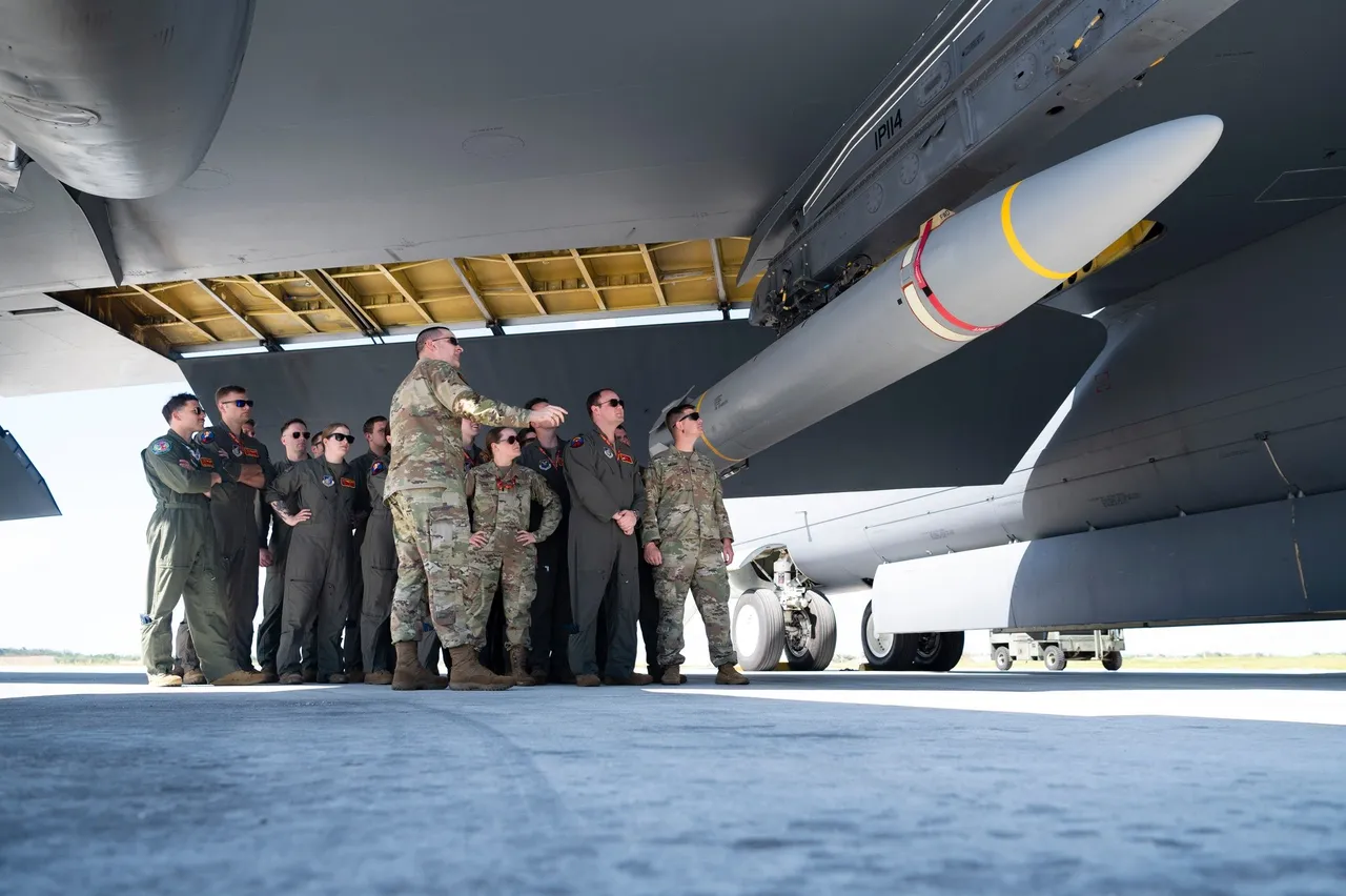 Airmen in flight suits and camouflage uniforms stand beneath a B-52 bomber wing as an instructor points to a long white missile mounted on a pylon
