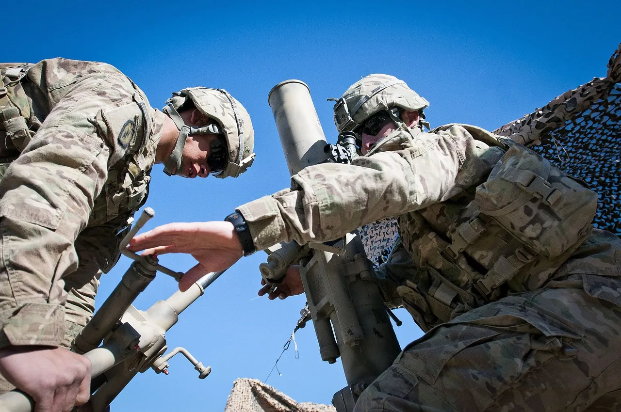 Two US Army soldiers adjust the aim of a 120mm mortar tube outdoors