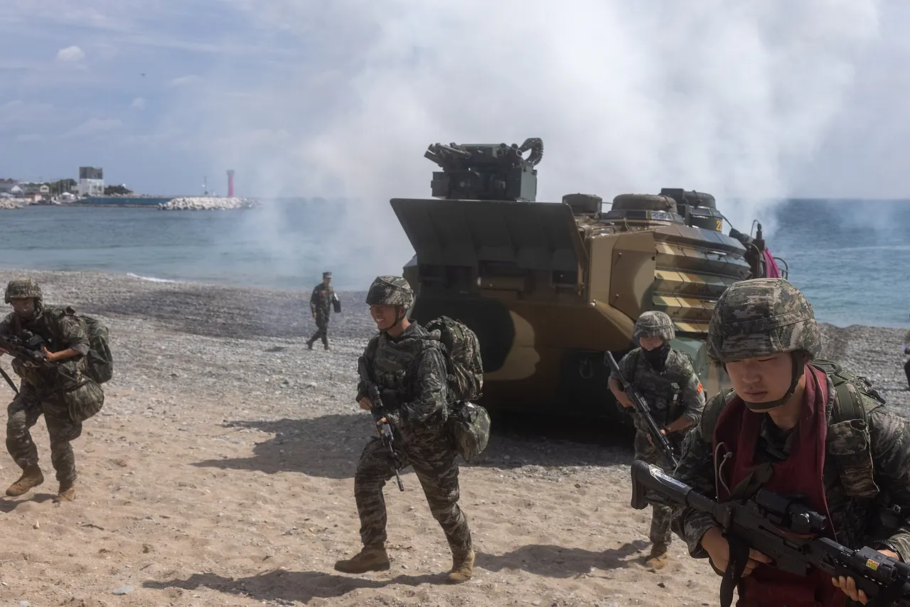 South Korean marines in camouflage carrying rifles walk up a pebbly beach away from a tracked amphibious assault vehicle, with smoke drifting over the sea behind them