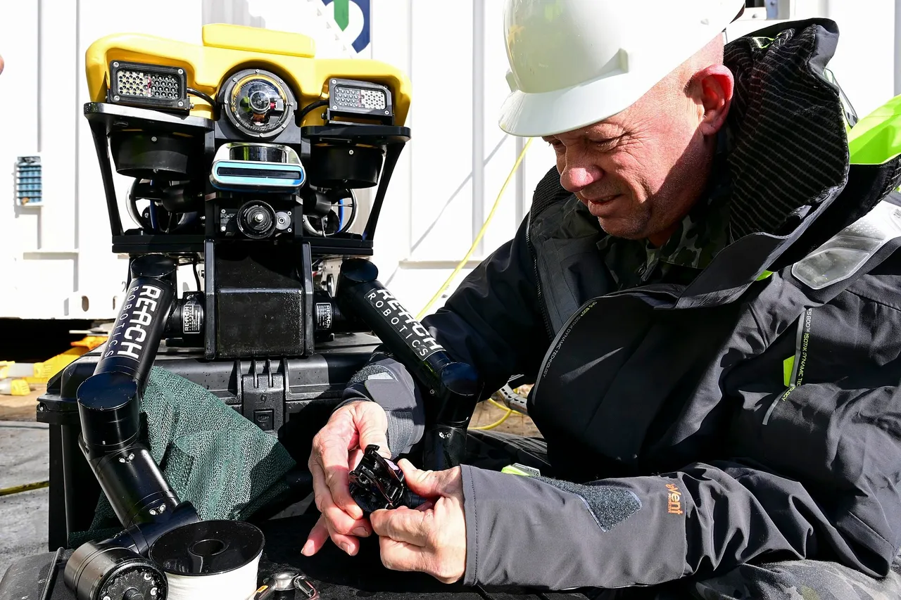 A sailor in a hard hat and life vest working on a yellow underwater robot on the deck of a ship
