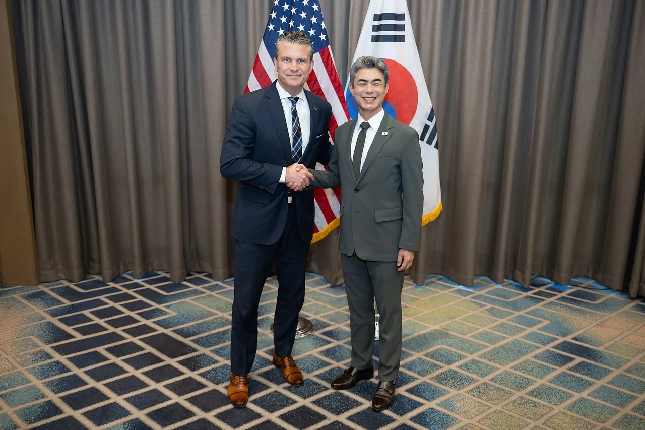 Pete Hegseth and Kang Shin-chul shaking hands in front of US and South Korean flags