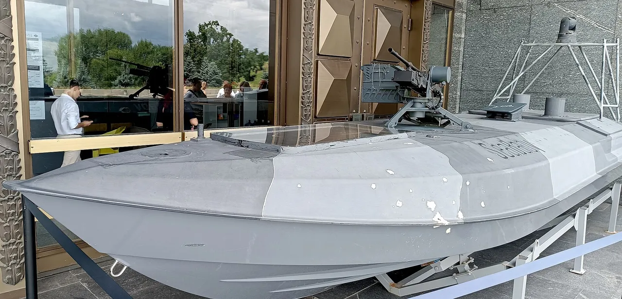 A grey Ukrainian drone boat with a mounted machine gun on a display stand at a museum entrance