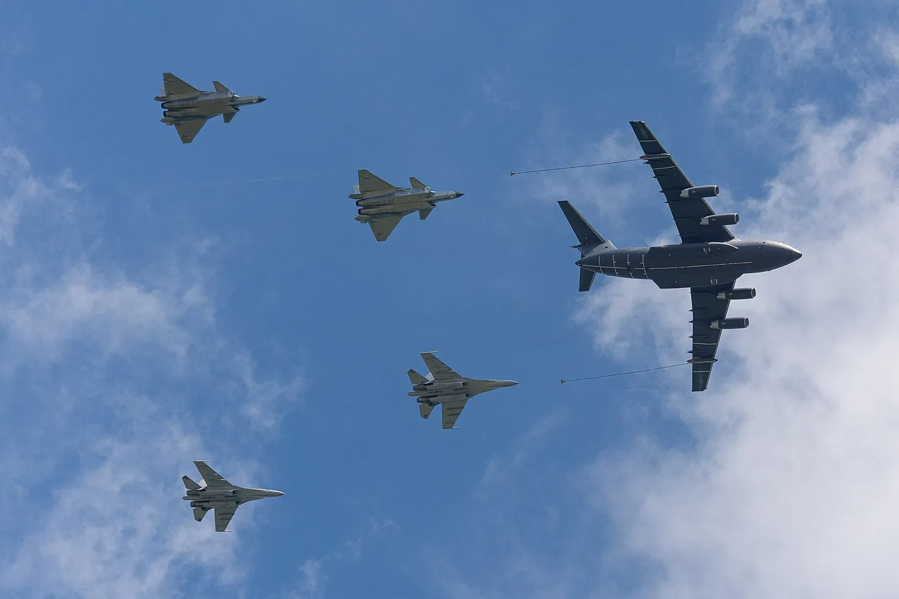 A large four-engine grey tanker aircraft trailing two refuelling hoses flies beside four fighter jets against a blue sky