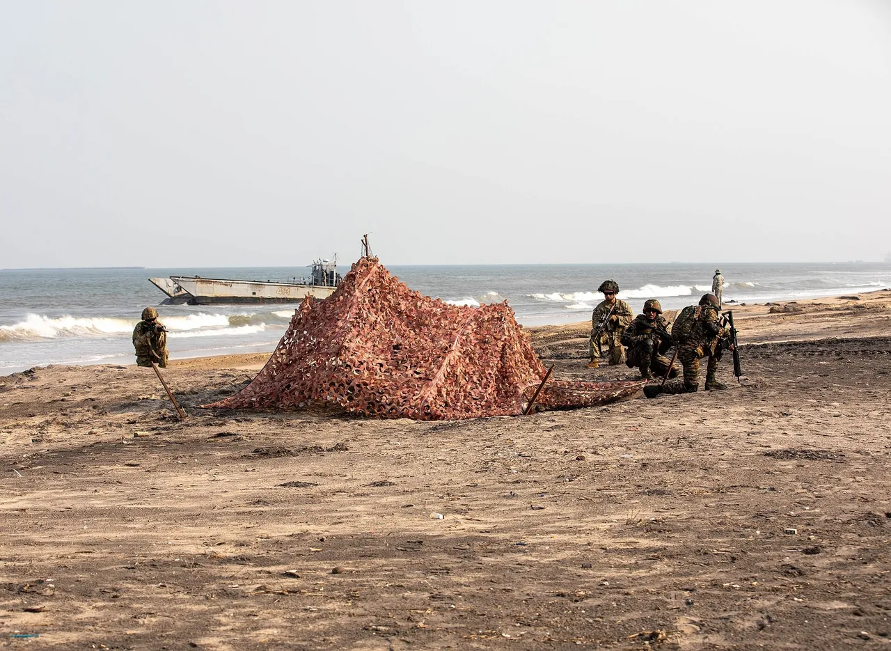Indian Army soldiers in camouflage taking up firing positions on a sandy beach during an amphibious landing drill