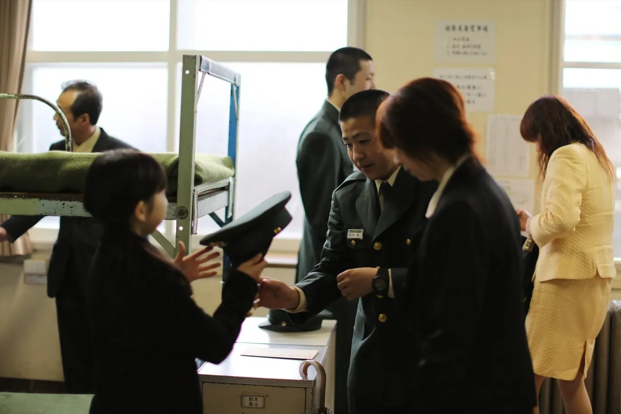 Rows of young Japanese army recruits in green uniforms standing in formation at an indoor enlistment ceremony