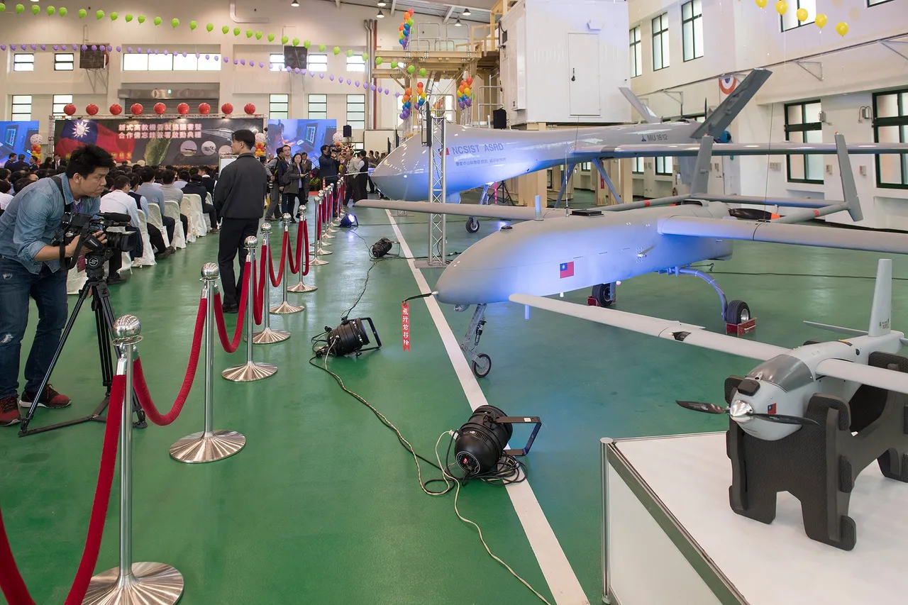 Grey Taiwanese-built military drones with long wings displayed in a hangar beside a red rope barrier as a cameraman films