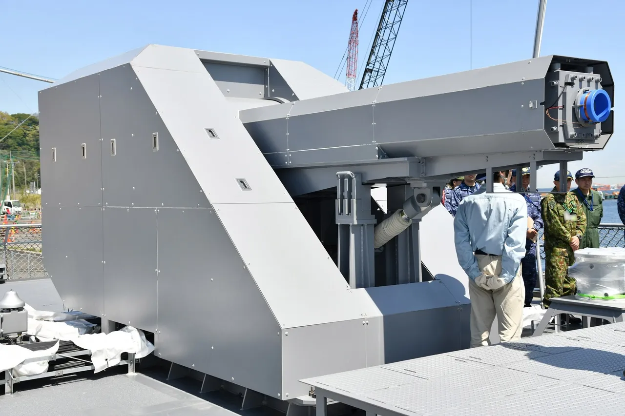 A grey angular railgun turret with a long barrel mounted on the deck of a Japanese naval test ship
