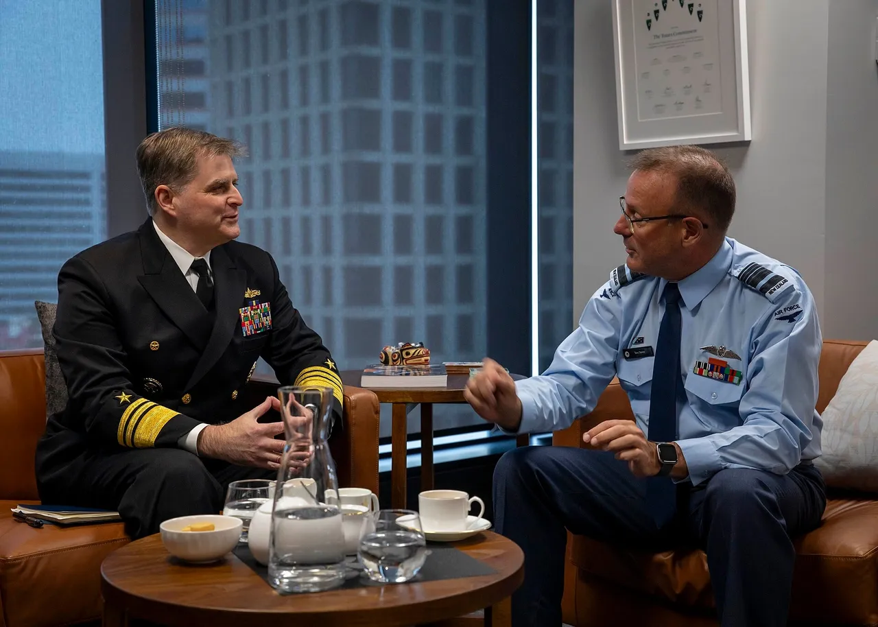 A U.S. Navy admiral in dark uniform and a New Zealand air marshal in a light blue shirt talking in armchairs in an office