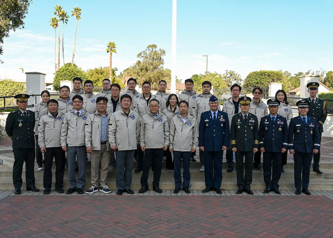 A group of South Korean officials in grey jackets and military officers in dress uniforms stand in rows on steps outside a building with palm trees behind them