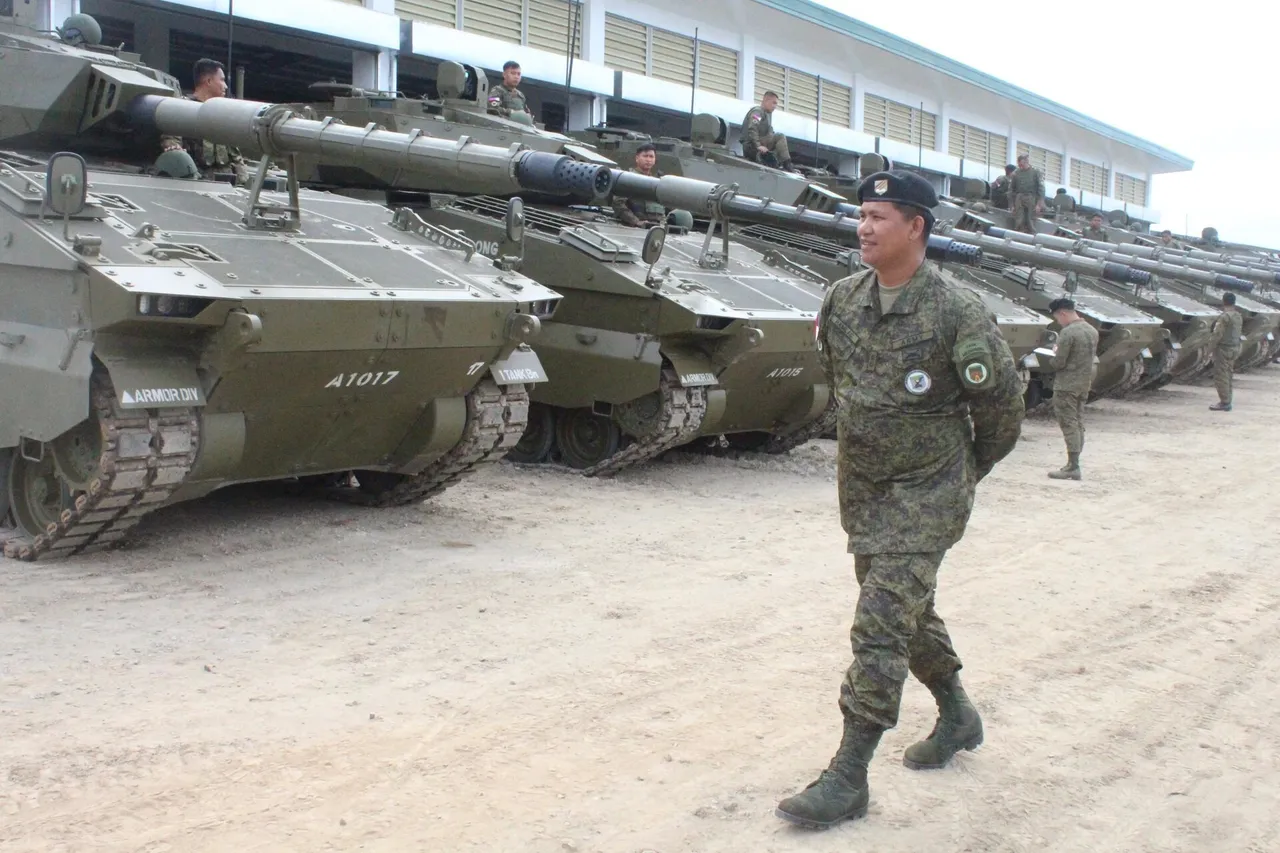 A row of green tracked light tanks with long guns parked in front of a building as a soldier in camouflage walks past