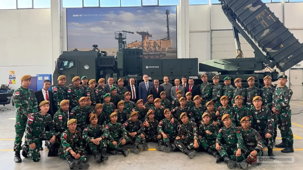 Rows of Indonesian soldiers in camouflage and berets pose in a factory hall in front of a green military truck carrying a raised missile launcher