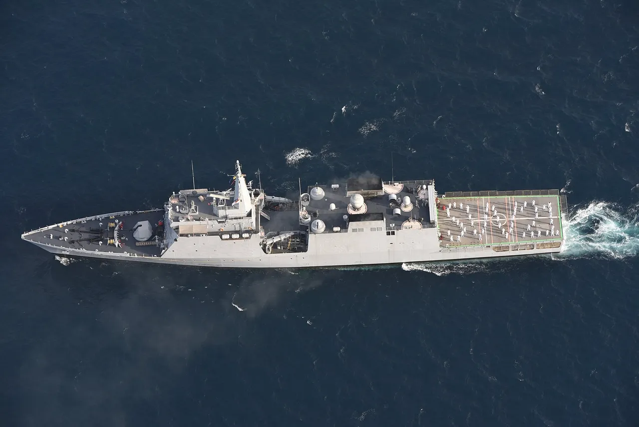 Overhead view of a grey Indian Navy patrol ship with a helicopter deck at its stern sailing through blue water