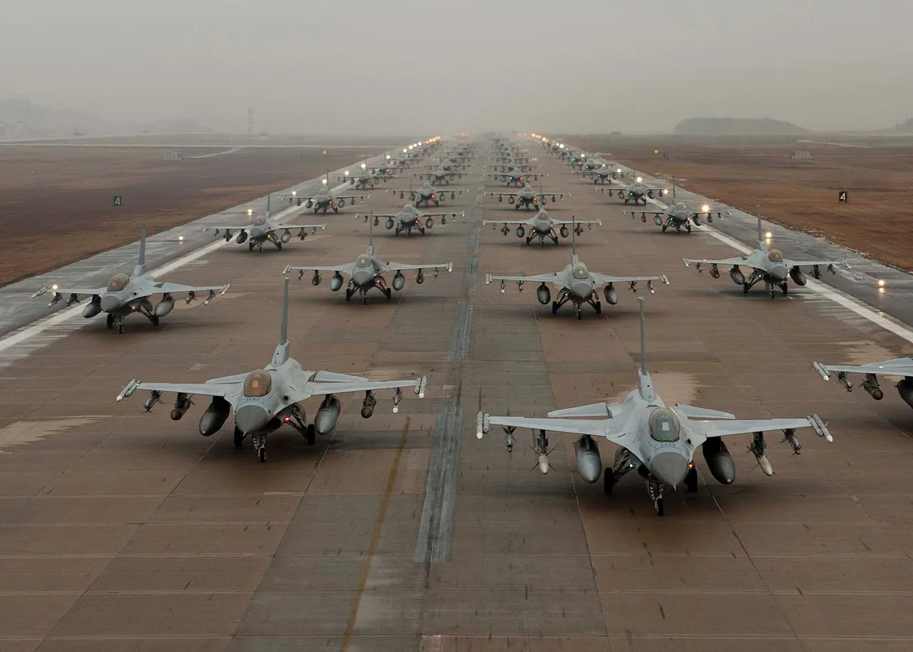A long line of grey F-16 fighter jets taxiing nose to tail along an airfield runway on a clear day