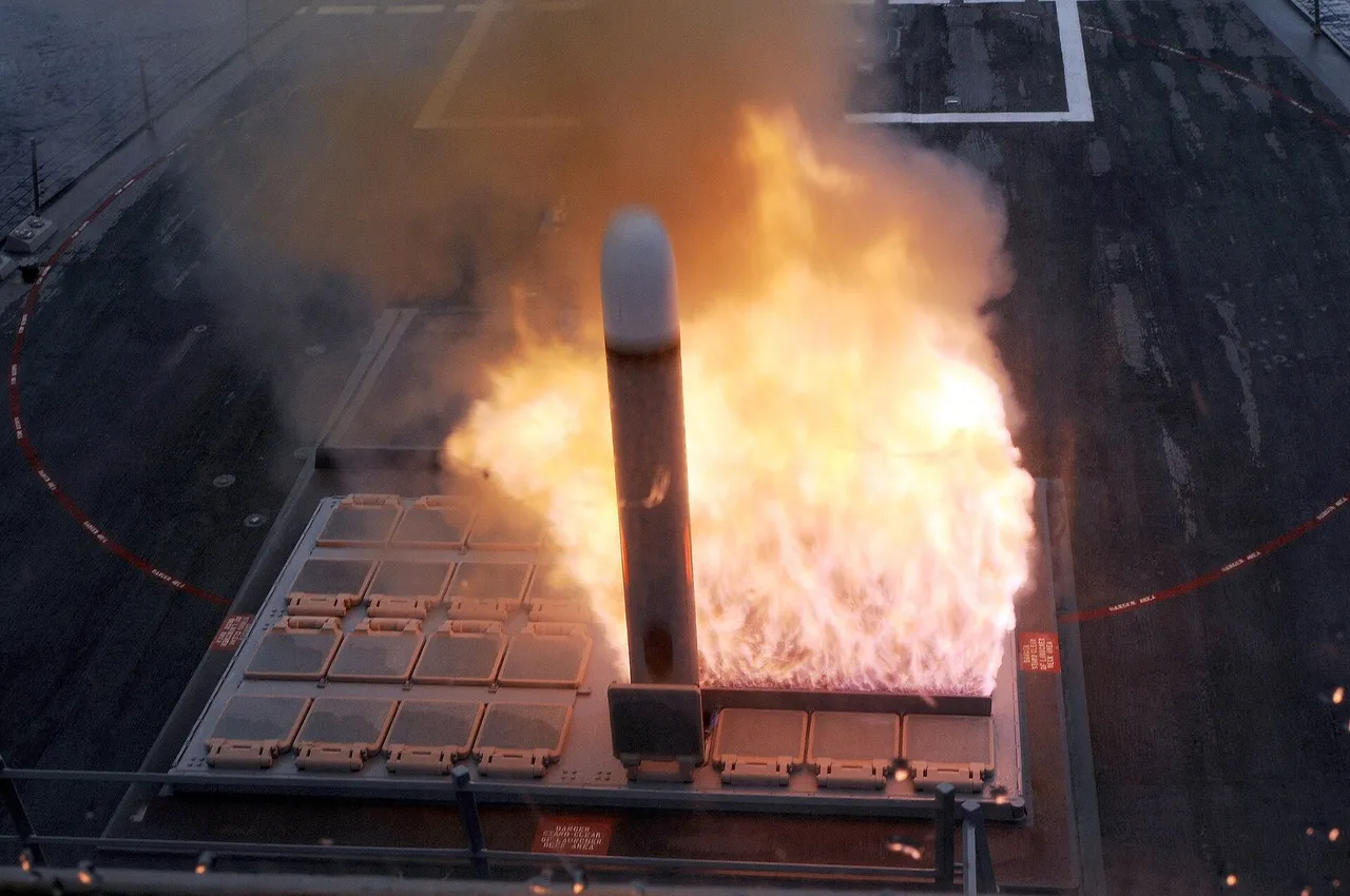 A Tomahawk cruise missile rising out of a vertical launch cell on a warship deck amid a burst of orange flame and smoke