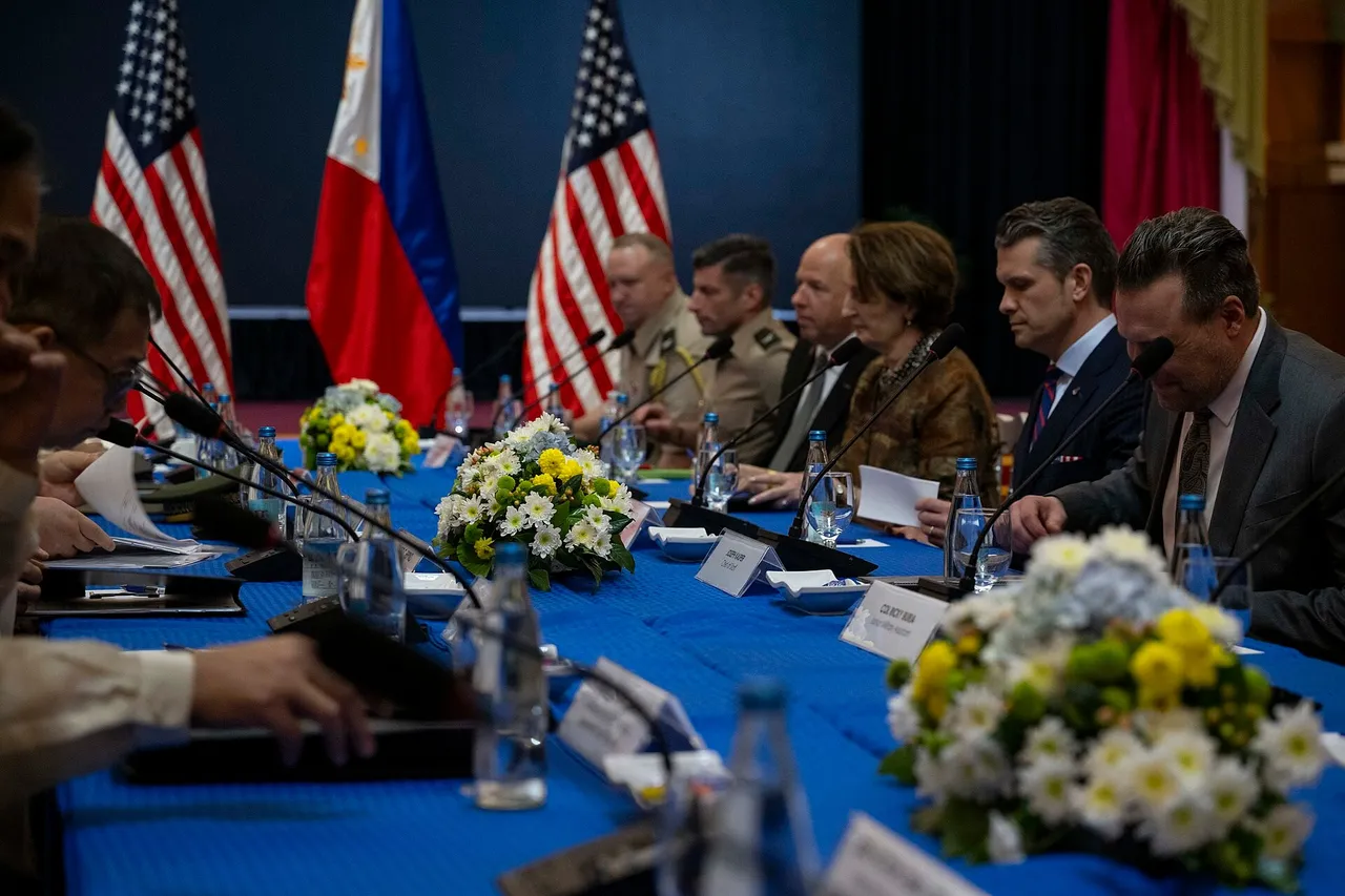 US and Philippine officials sit facing each other at a long blue-covered table with flowers, microphones and national flags behind them