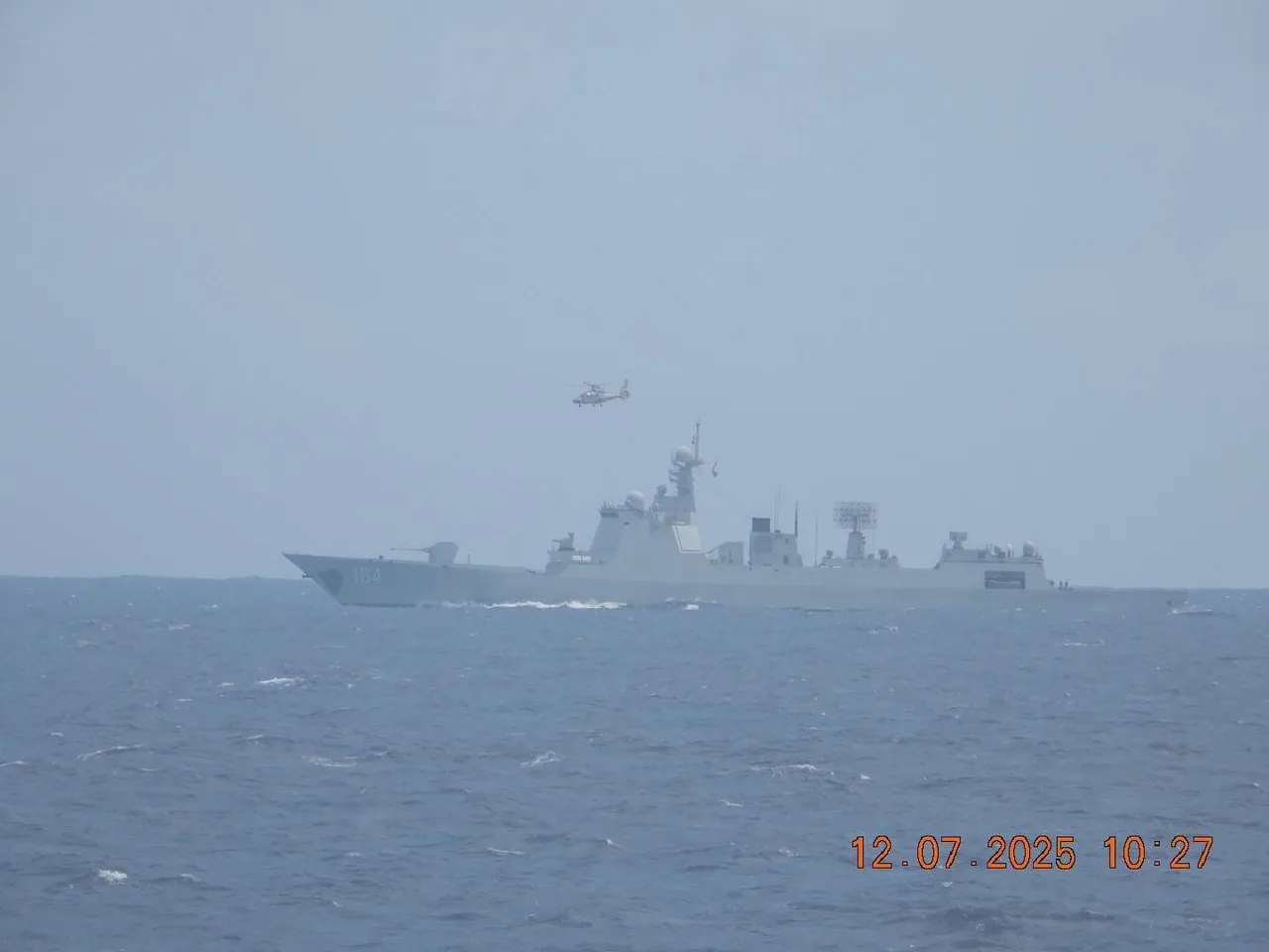 A grey Chinese navy warship at sea with a small naval helicopter flying nearby