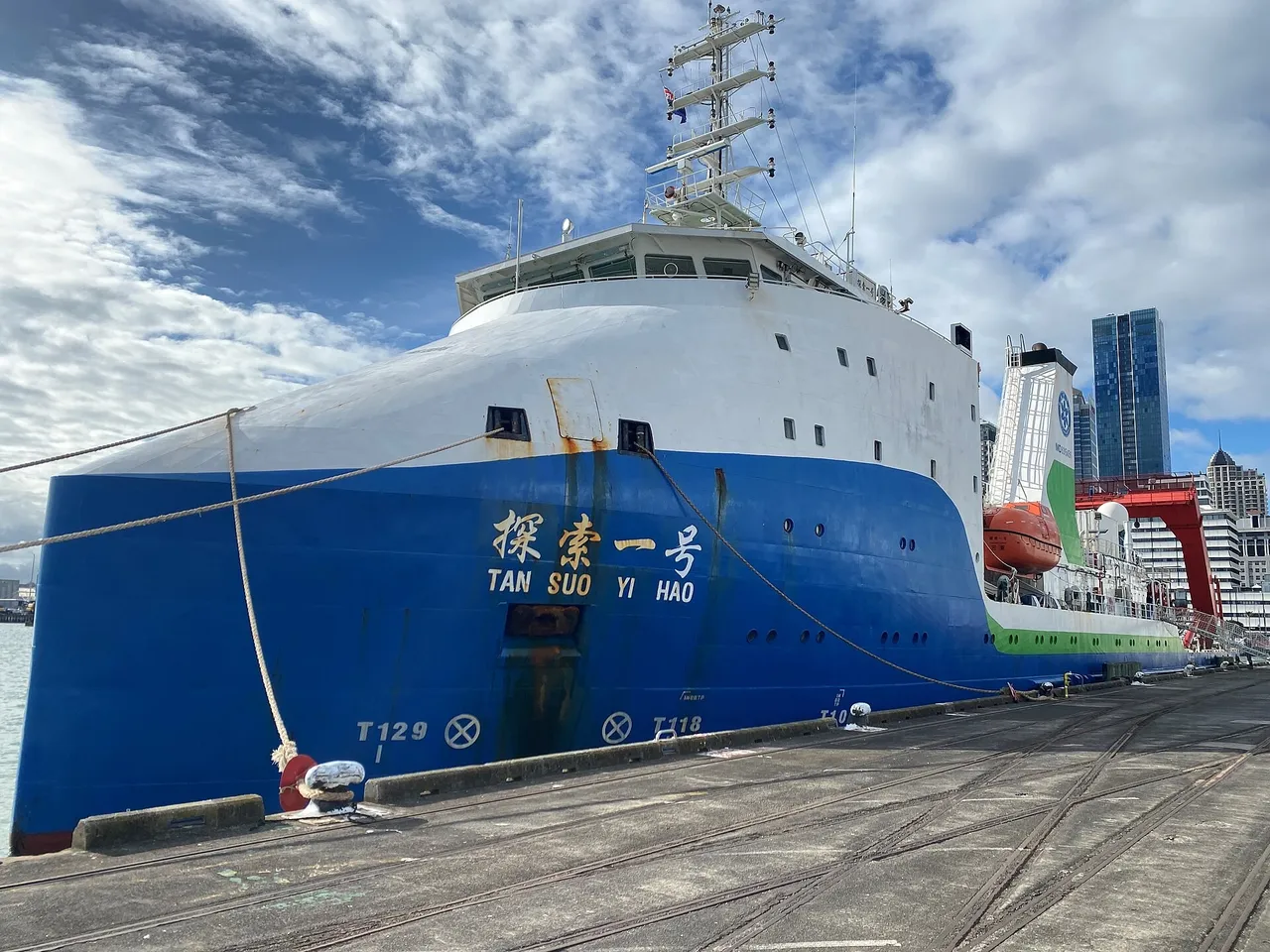 A blue-hulled research ship with a white superstructure and the name Tan Suo Yi Hao painted on its bow, moored at a quay