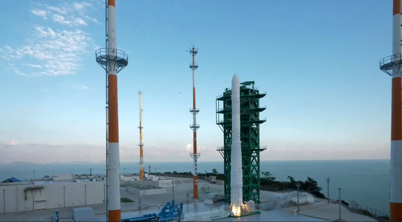 A white Nuri rocket ignites beside a green launch tower at a seaside launch pad framed by red and white lightning masts