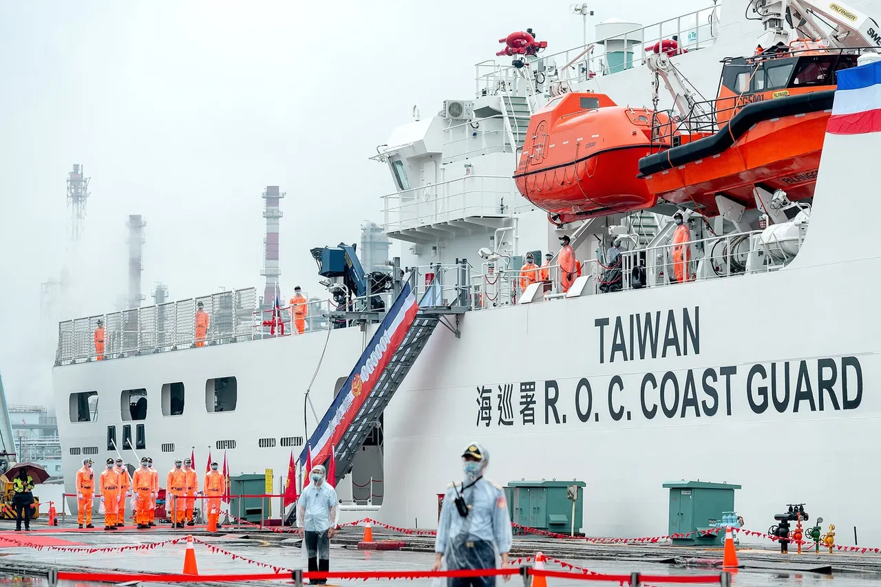 A large white coast guard ship marked Taiwan R.O.C. Coast Guard, with orange lifeboats on its side, as crew in orange uniforms line up on the quay beside it.