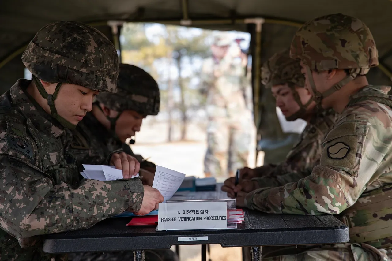 South Korean soldiers in digital camouflage and US soldiers sit at a table in a tent reviewing transfer verification documents