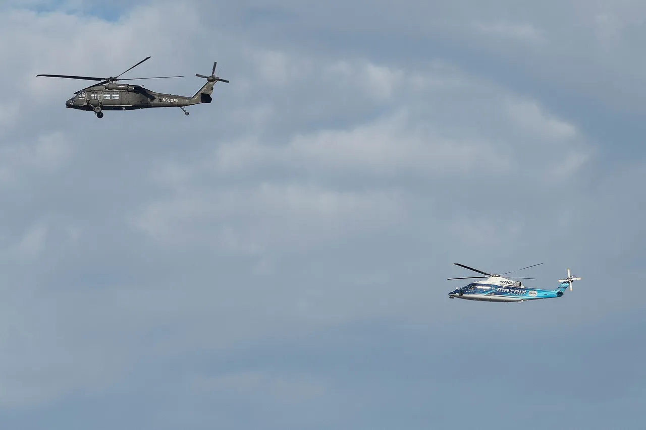 A Black Hawk helicopter and a smaller white Sikorsky S-76 helicopter flying side by side over water