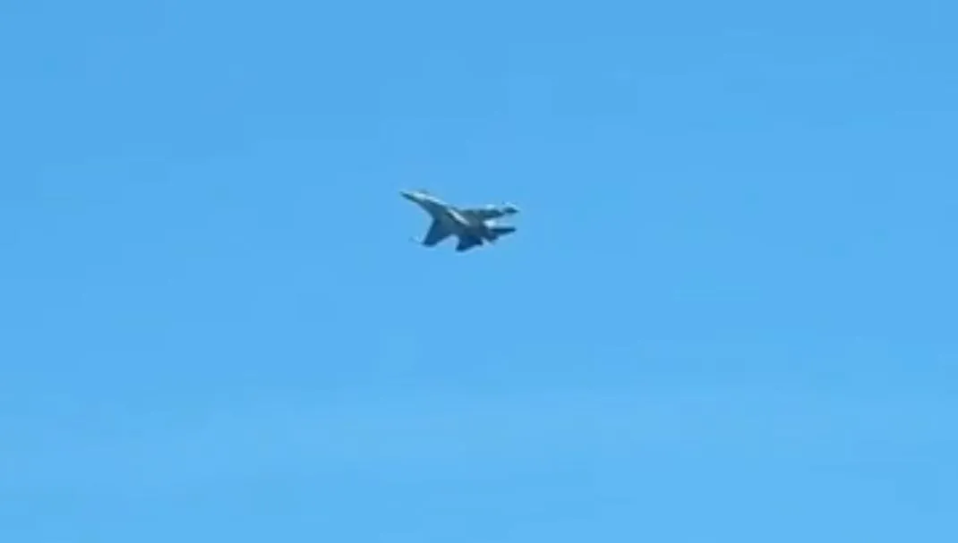 A twin-tail fighter jet seen from below against a clear blue sky