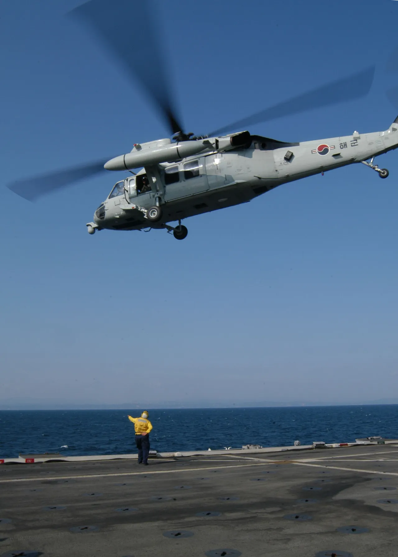 A grey Black Hawk helicopter hovers low over the flight deck of a navy ship at sea