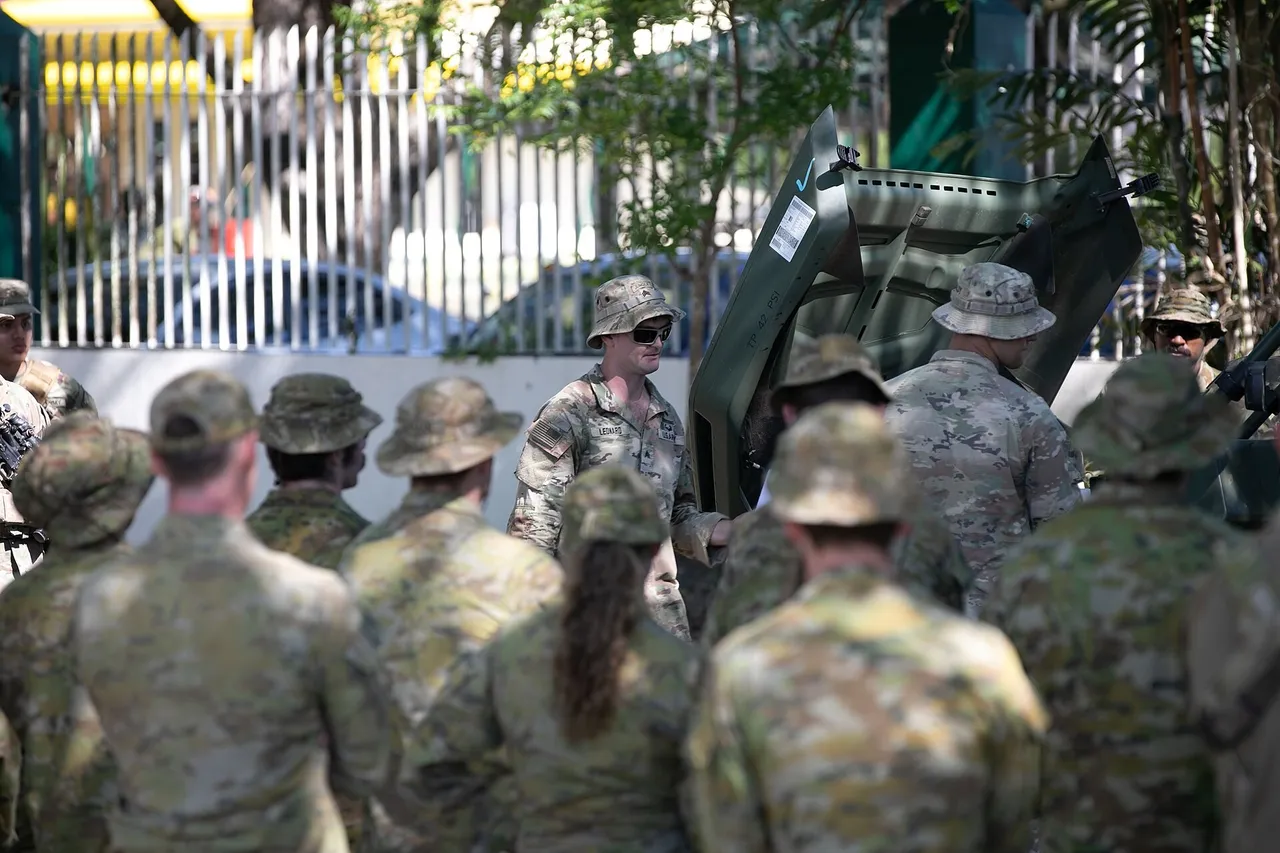 A US Army soldier stands beside an open-topped Infantry Squad Vehicle explaining it to Australian soldiers at a training base