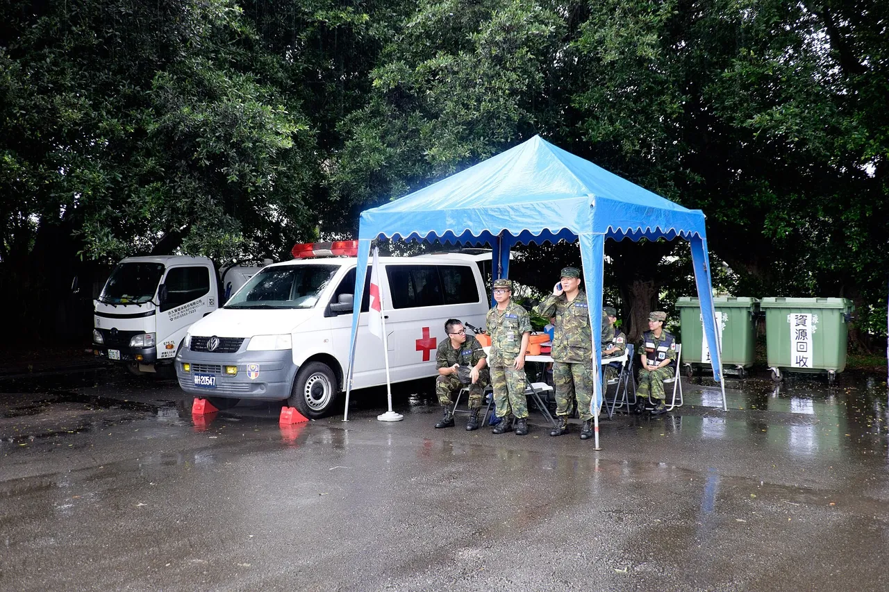 Soldiers in camouflage uniforms under a blue tent next to a white military ambulance with a red cross