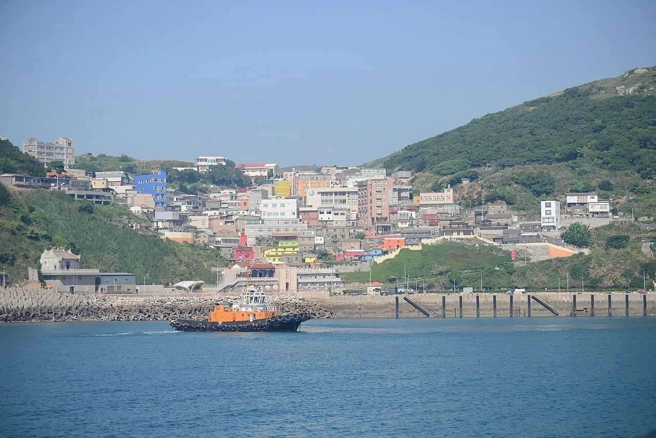 Hillside village above the harbour at Dongyin in Matsu, with an orange tugboat crossing the water in the foreground.