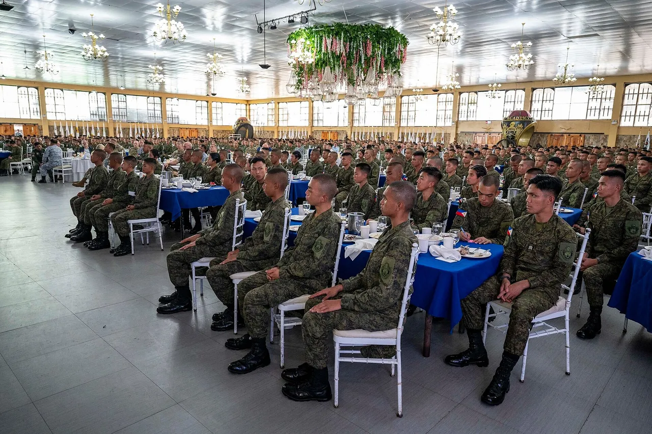 Rows of Philippine Military Academy cadets in camouflage uniforms seated at tables with blue cloths in a large hall with chandeliers