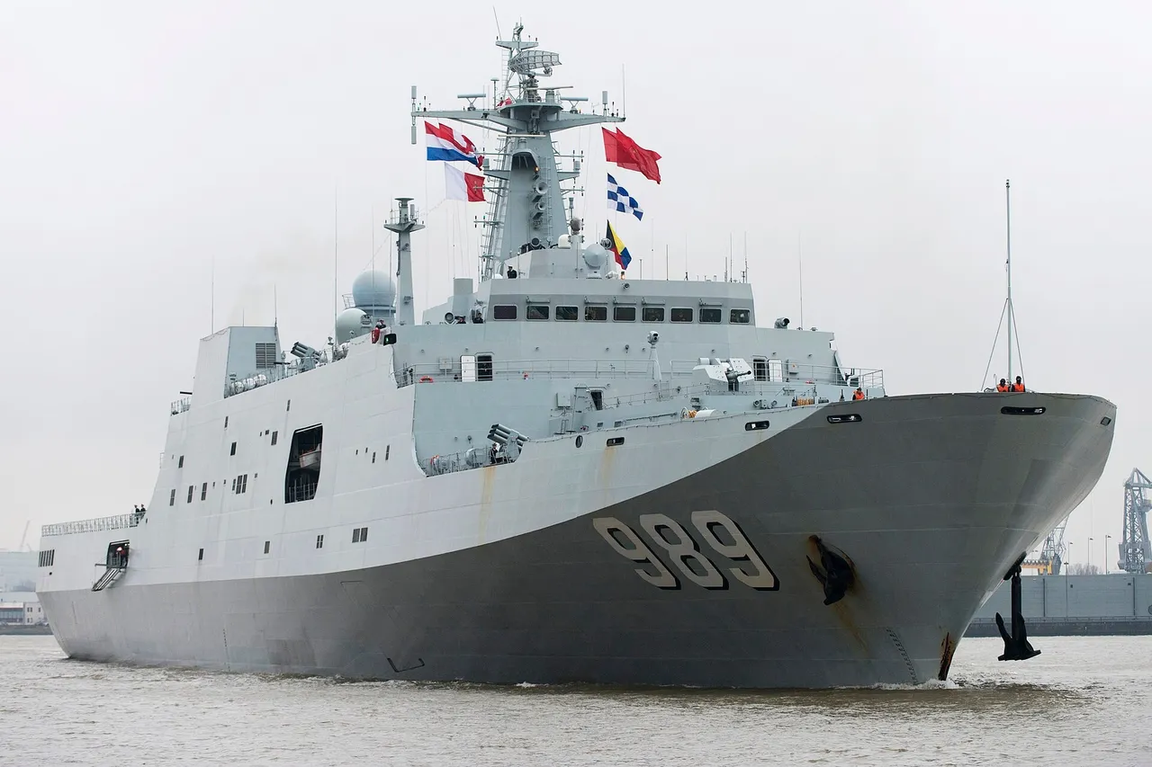 A large grey Chinese navy amphibious ship with hull number 989 sails through a harbour flying several flags