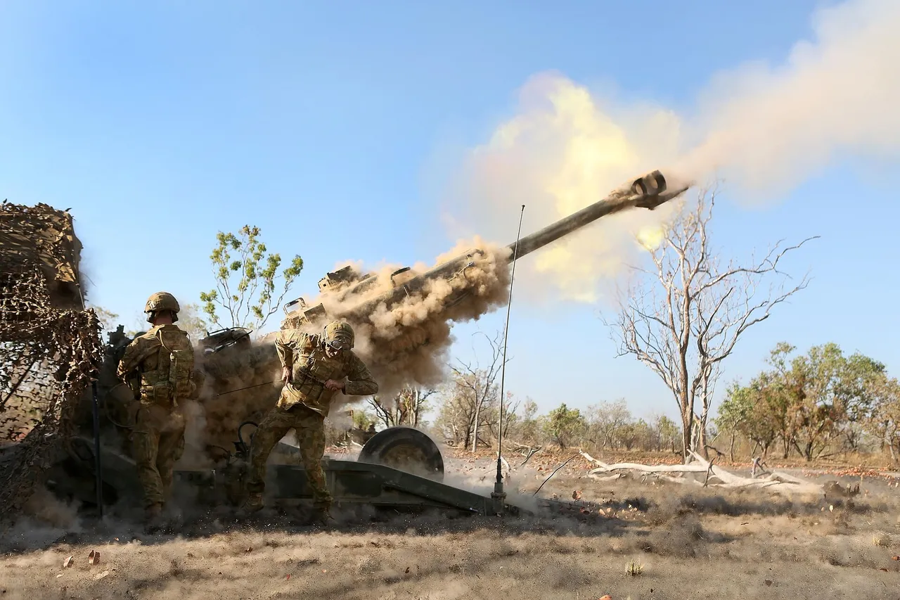 Australian soldiers in camouflage fire a towed M777 howitzer in dry scrubland, with smoke from the muzzle.
