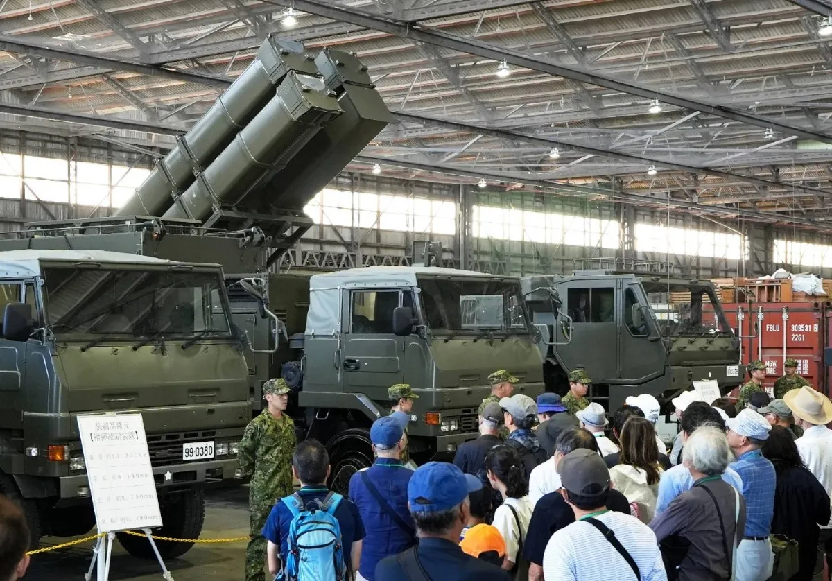Crowd of visitors in a hangar looking at olive-green military trucks, one with raised missile launch canisters