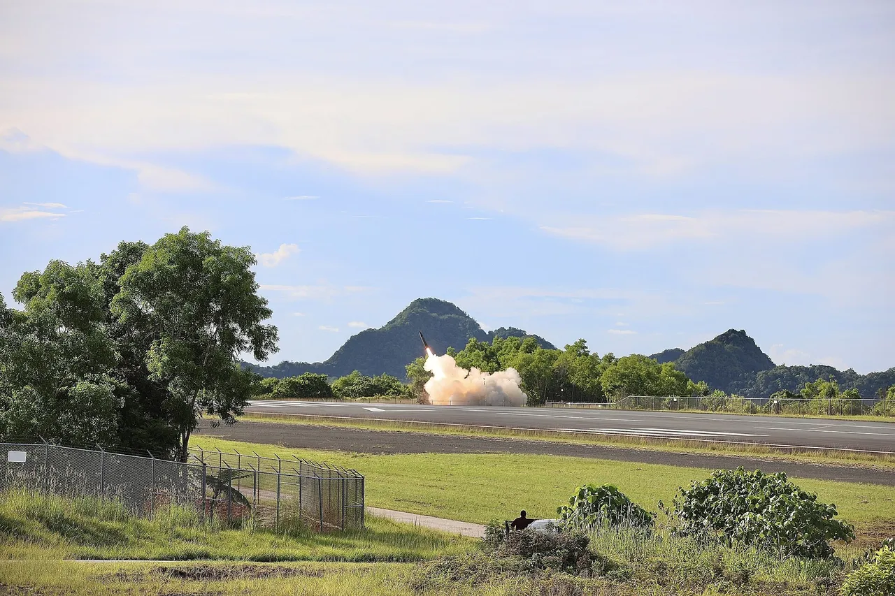 A missile climbs from a launcher on an airfield in Palau, leaving a white smoke cloud in front of green hills