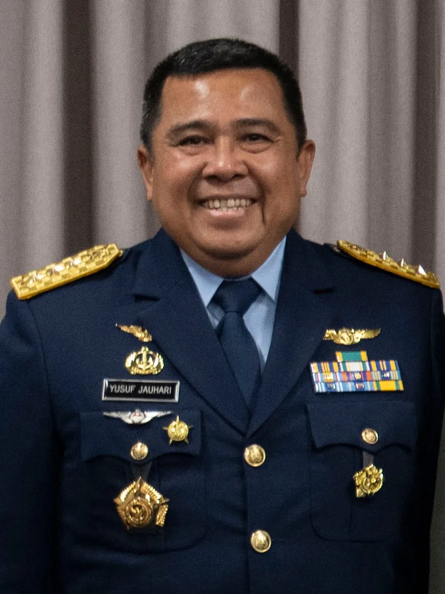 Portrait of a smiling Indonesian air force officer in a dark blue dress uniform with gold shoulder boards and a name tag reading Yusuf Jauhari