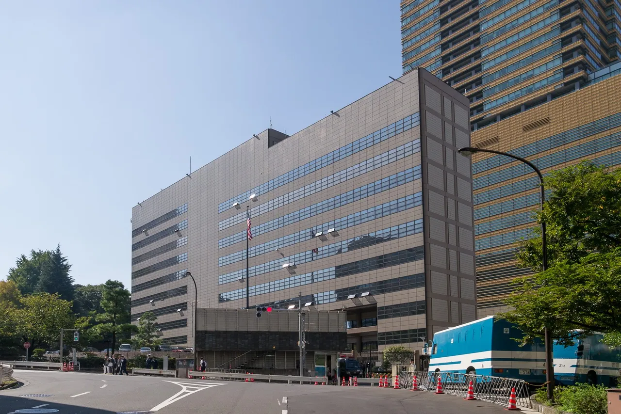 The grey multi-storey US Embassy building in Tokyo with an American flag out front under a clear blue sky