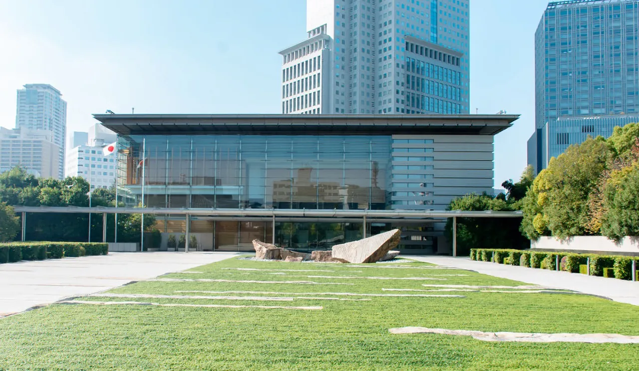 Modern glass and stone entrance of Japan's Prime Minister's Office building with a flat canopy and trees in front