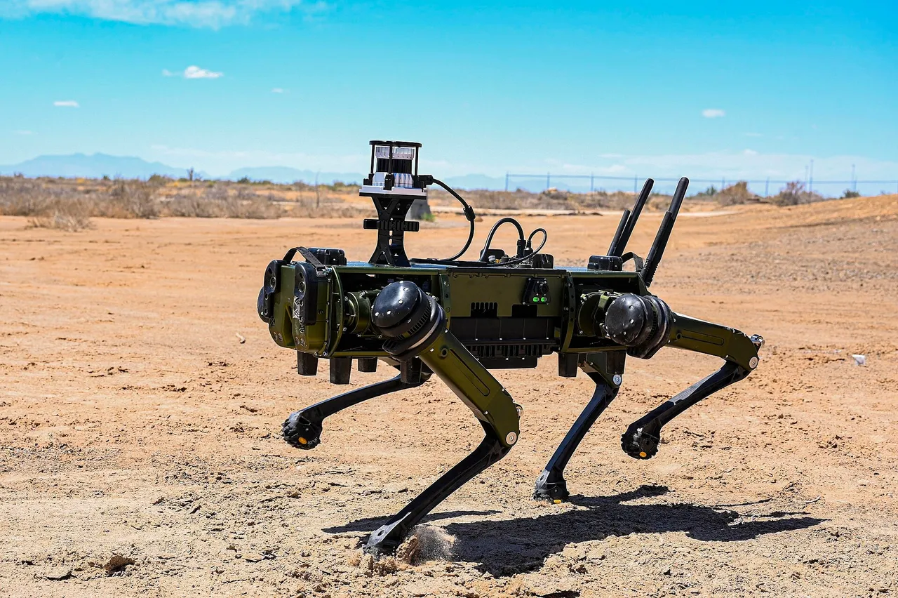 A dark green four-legged robot with a sensor mast and antennas walking across sandy desert ground