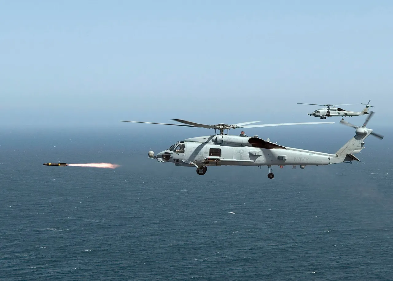 A grey US Navy MH-60R Seahawk helicopter flying low over the sea as a Hellfire missile streaks ahead of it, with a second helicopter in the background